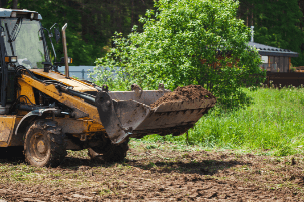 A yellow tractor hauling dirt, clearing off a property